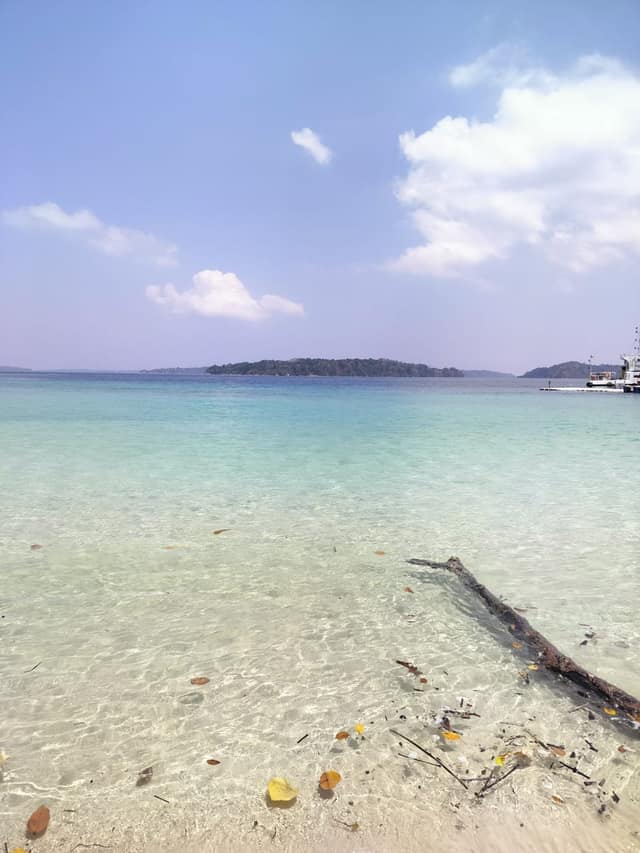 Glass-clear turquoise shallows at Kalapathar Beach with driftwood in the water, April 2024