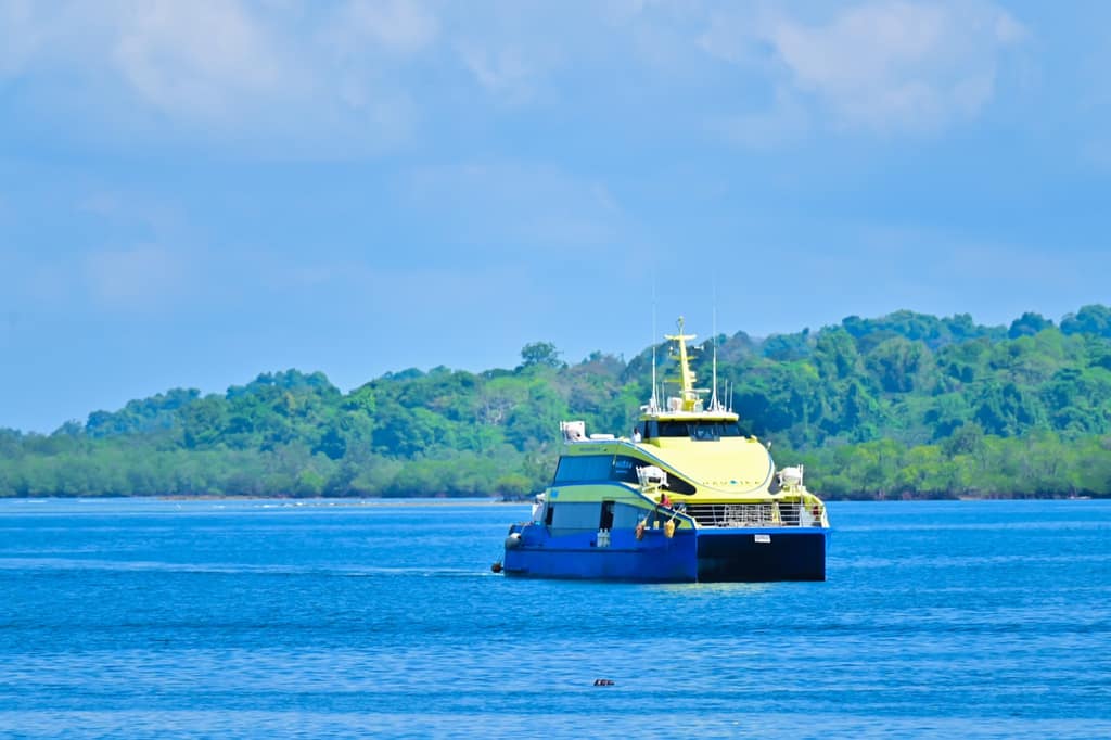 A private catamaran ferry on blue water off Port Blair with forested coastline behind